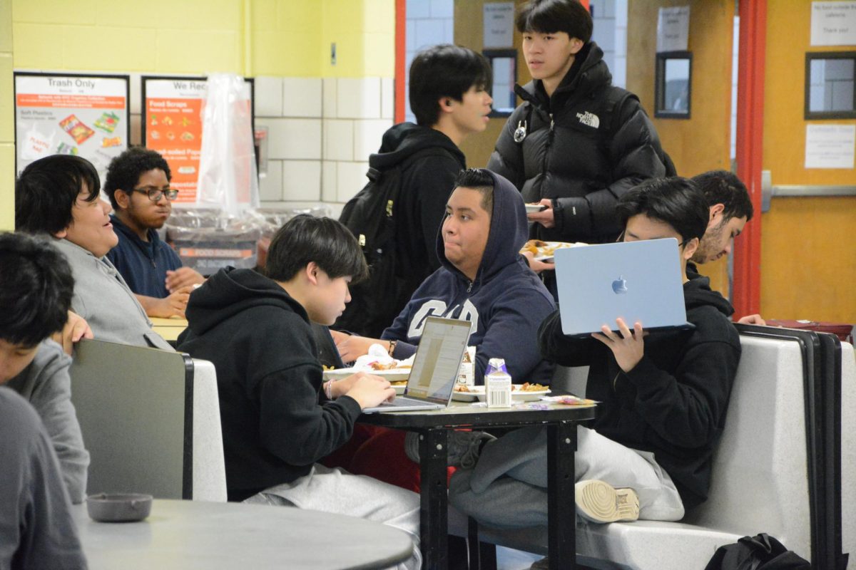 Even at a lunch table in the cafeteria, screens are present. Students on bench (l. to r.): Allen Liang, David Chen, Brian Luis Michaca, Danson Xiao (11th Grade). Behind bench (l. to r.): Ethan Wu and Alfred Li (11th Grade). 
